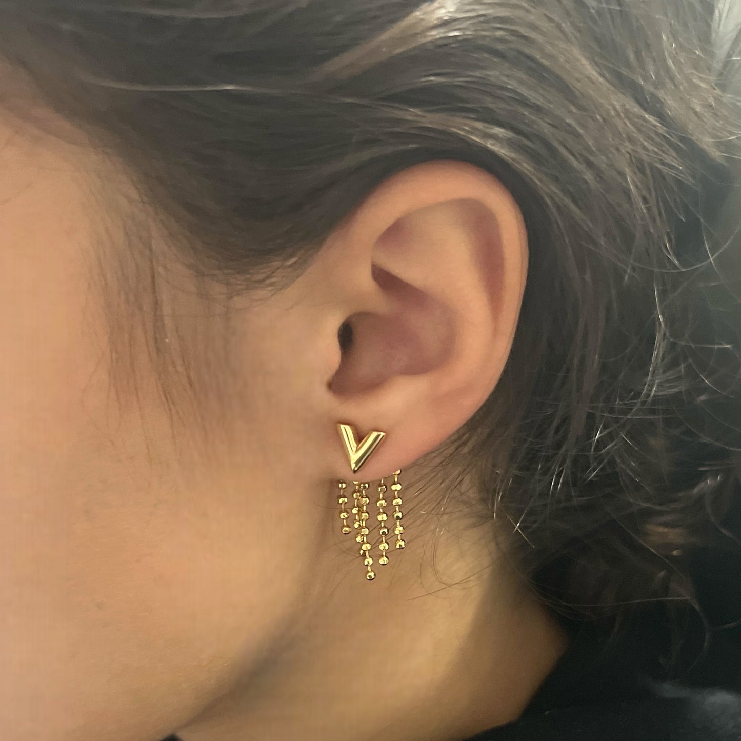Gold V tassel earrings worn on the ear, showcasing the elegant V-shaped design and chic dangling gold bead tassels in detail.