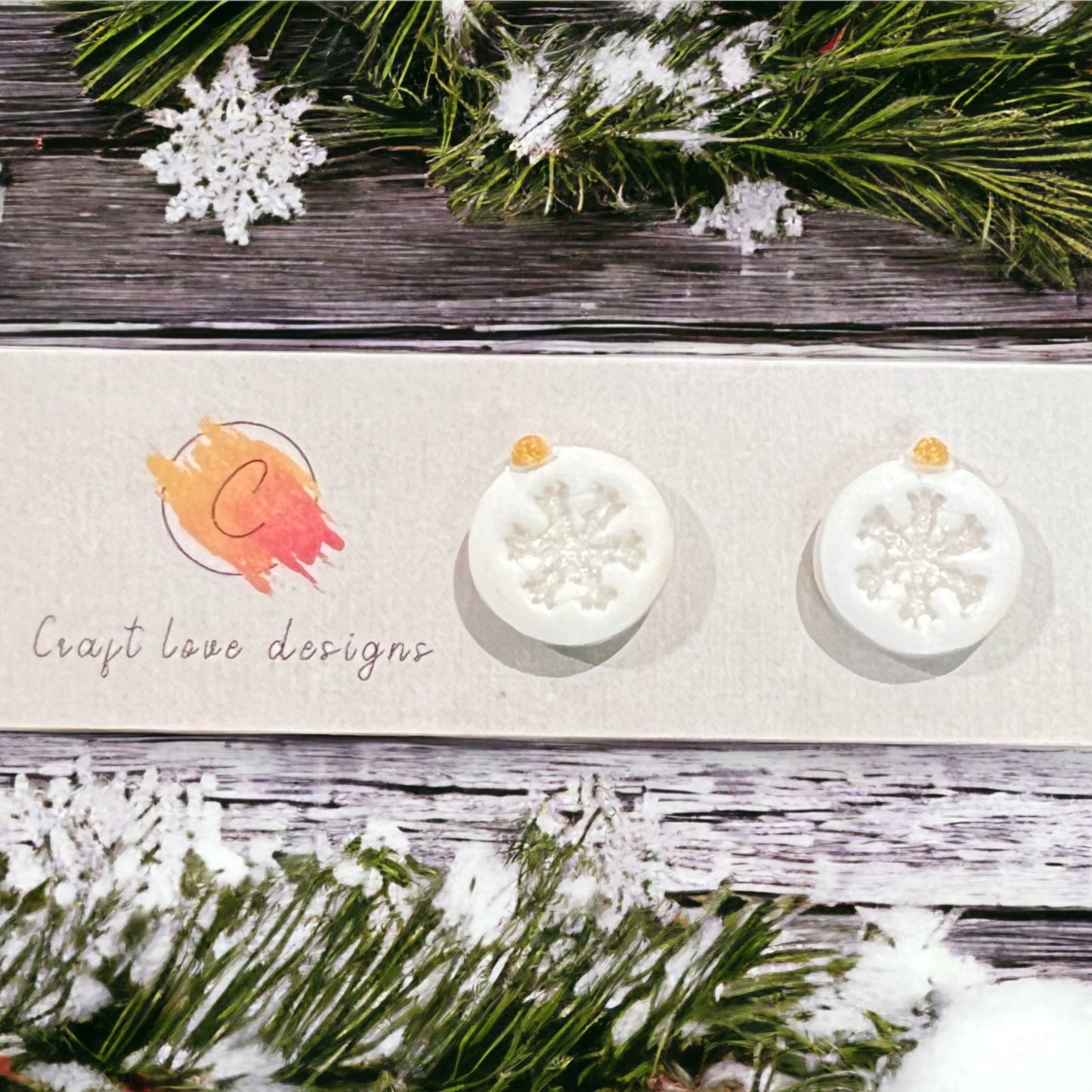 White snowflake ornament stud earrings with intricate frosty details, placed on a festive wooden surface surrounded by snowy decor.