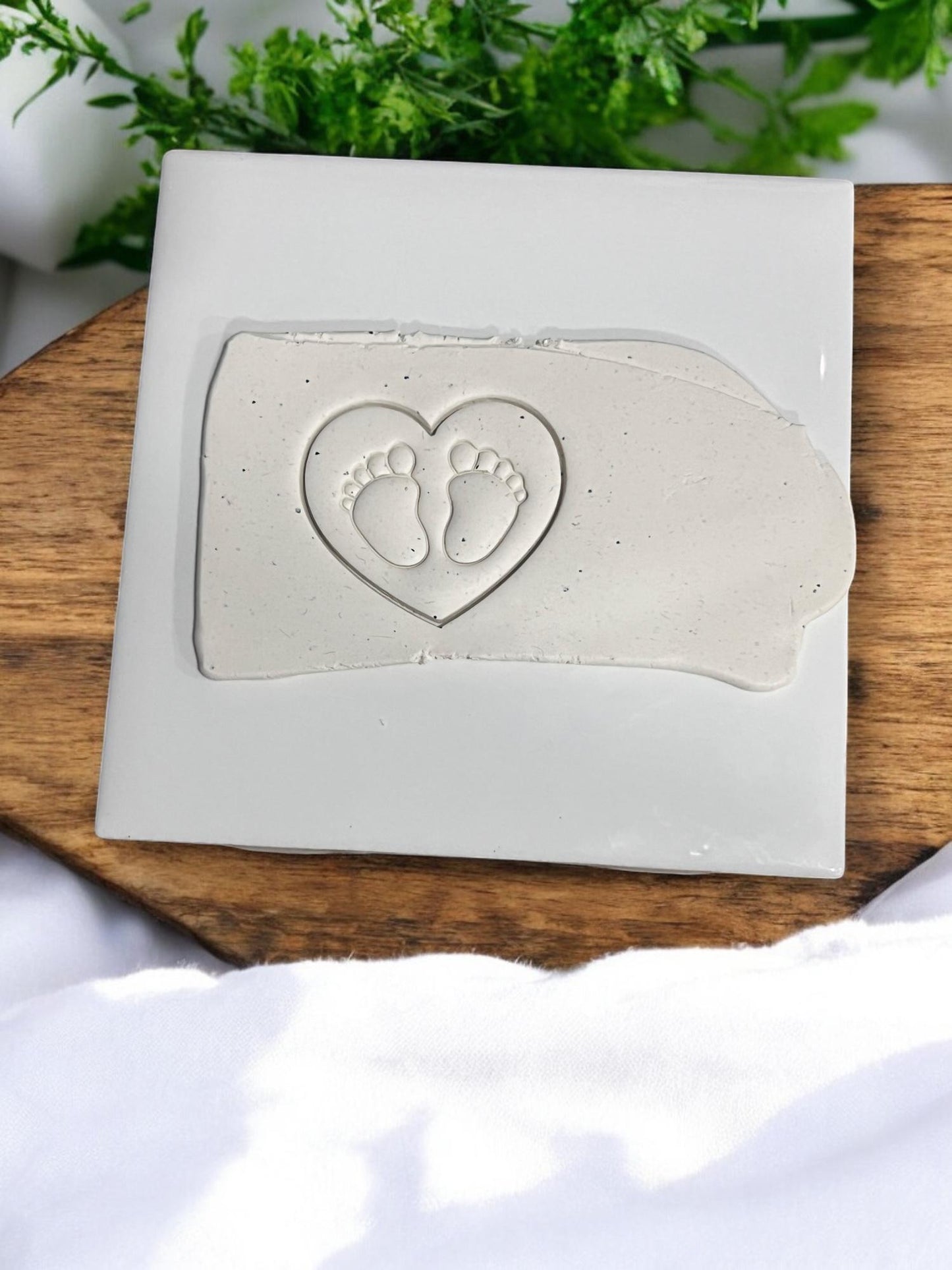 Baby feet heart cutter impression on light gray clay slab on ceramic tile