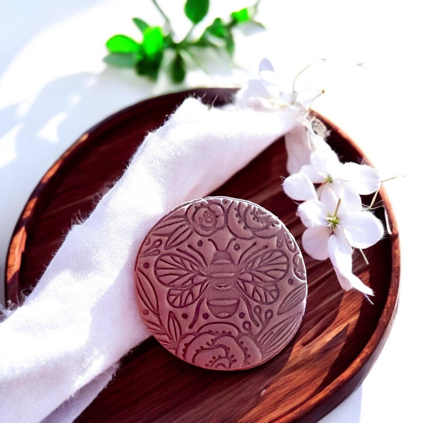A finished bee floral clay pendant styled on a wooden tray with fabric and flowers, perfect for statement jewelry photos