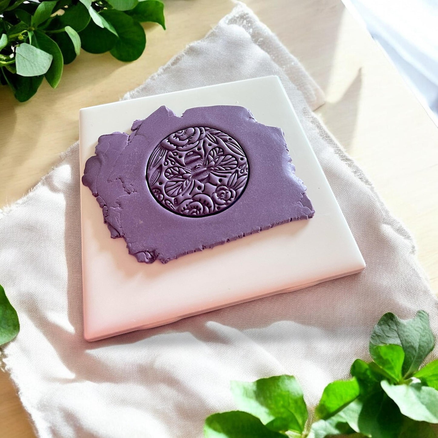 A detailed bee and floral imprint pressed into purple clay using a round polymer clay cutter, ideal for pendants or keychains