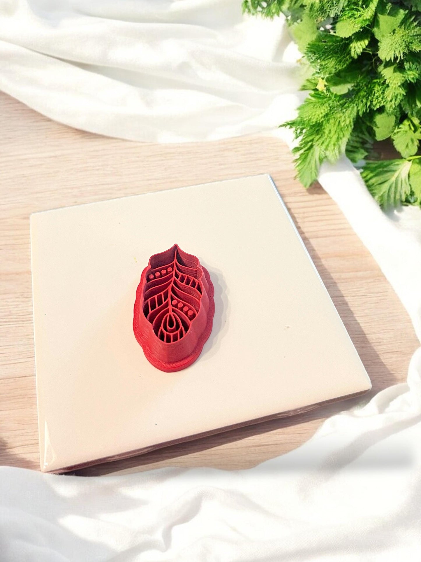 Red 3D printed cutter shaped like a feather or leaf with boho lines and texture, used for making 40mm polymer clay earrings
