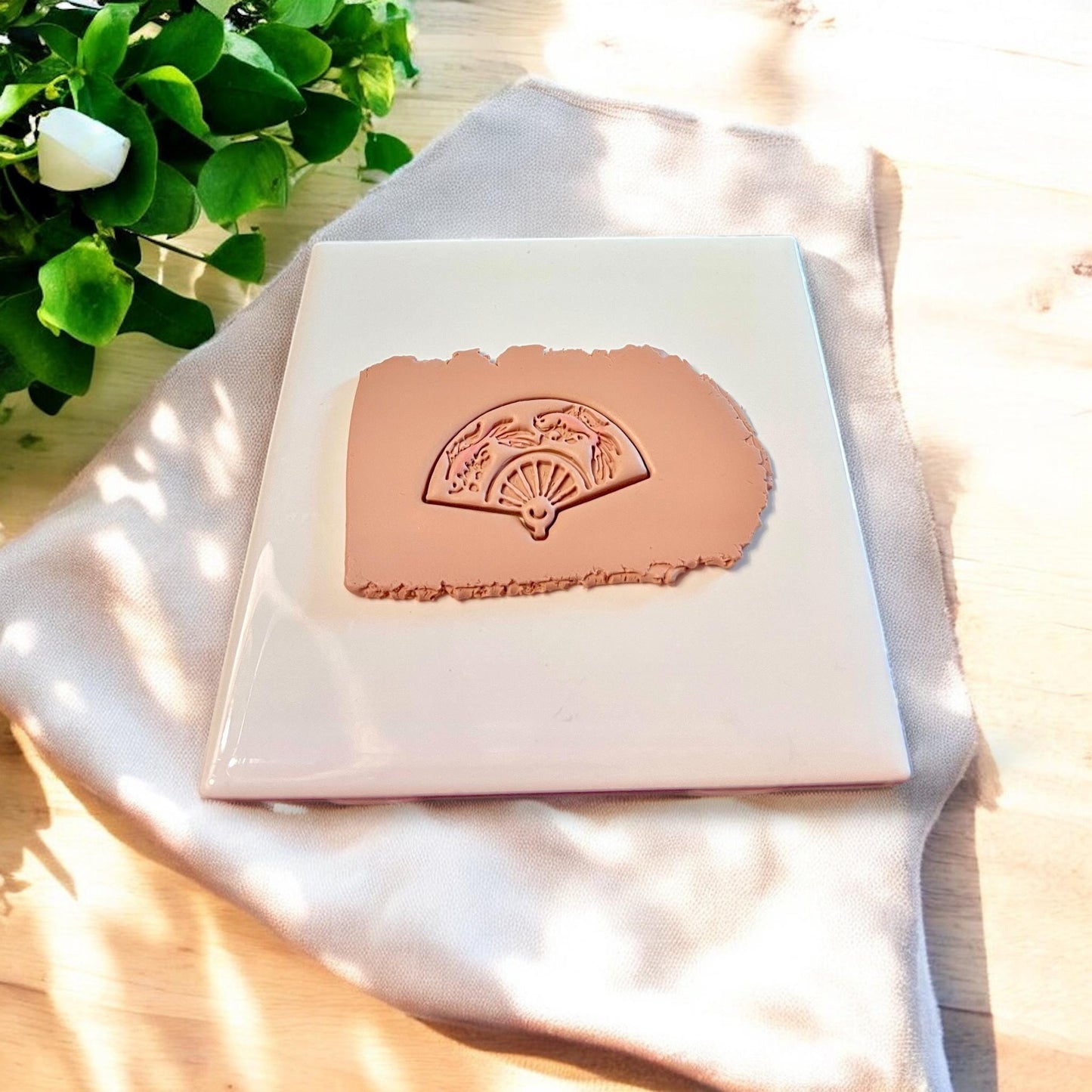 Clay slab stamped with detailed koi fan design from polymer clay cutter in soft tan clay