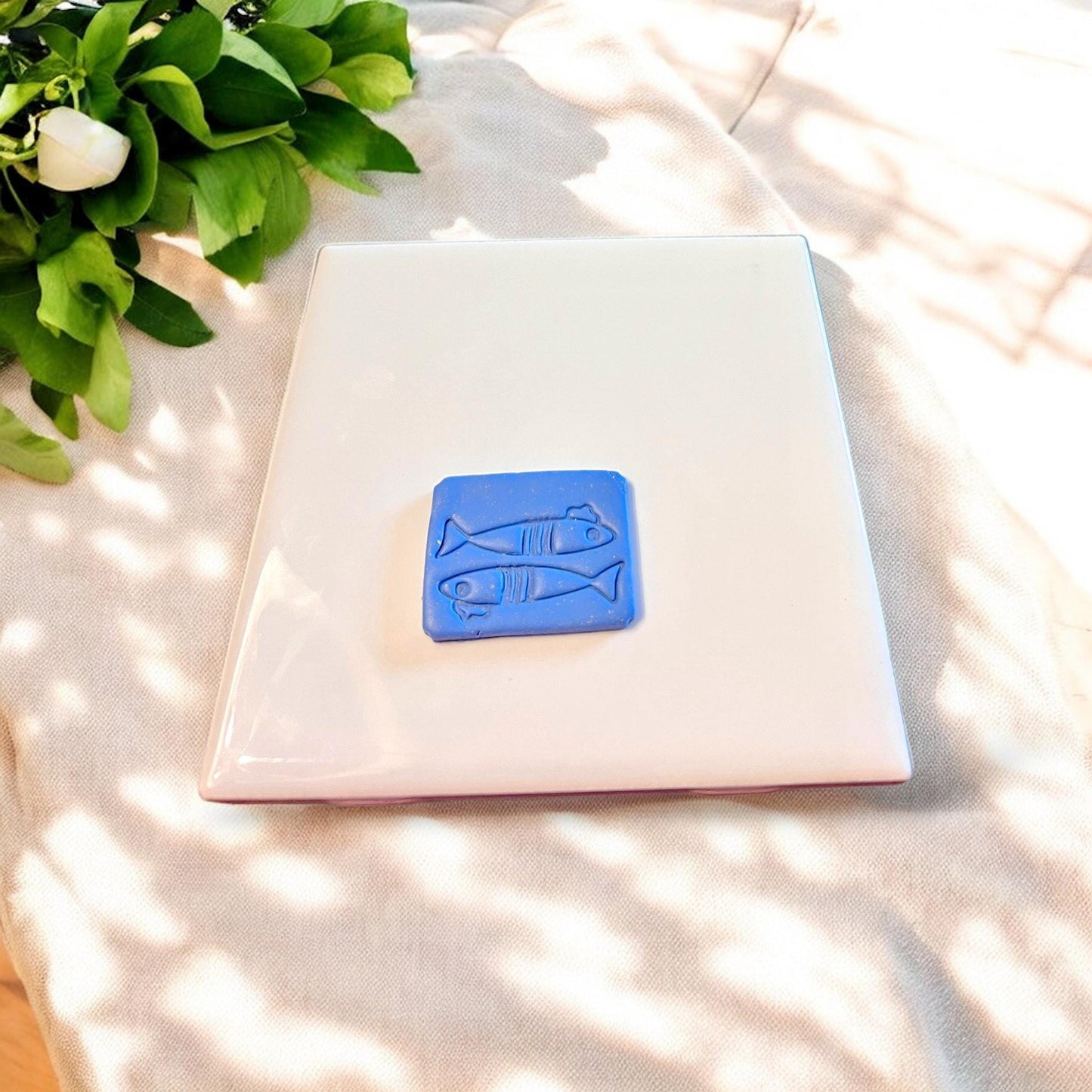 Small fish-shaped clay cutout with Parisian flair, designed for dangle earrings, placed centered on a clean ceramic tile