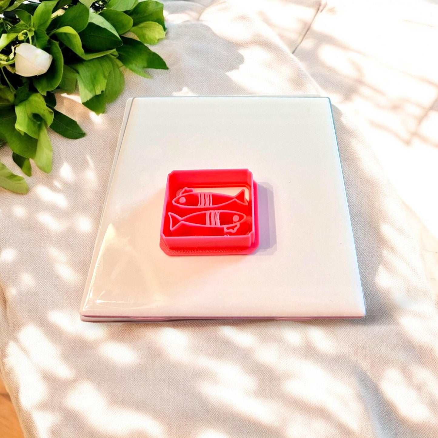 Red cutter shaped like a fish with beret detail, shown upright on white tile surrounded by natural daylight and soft fabric