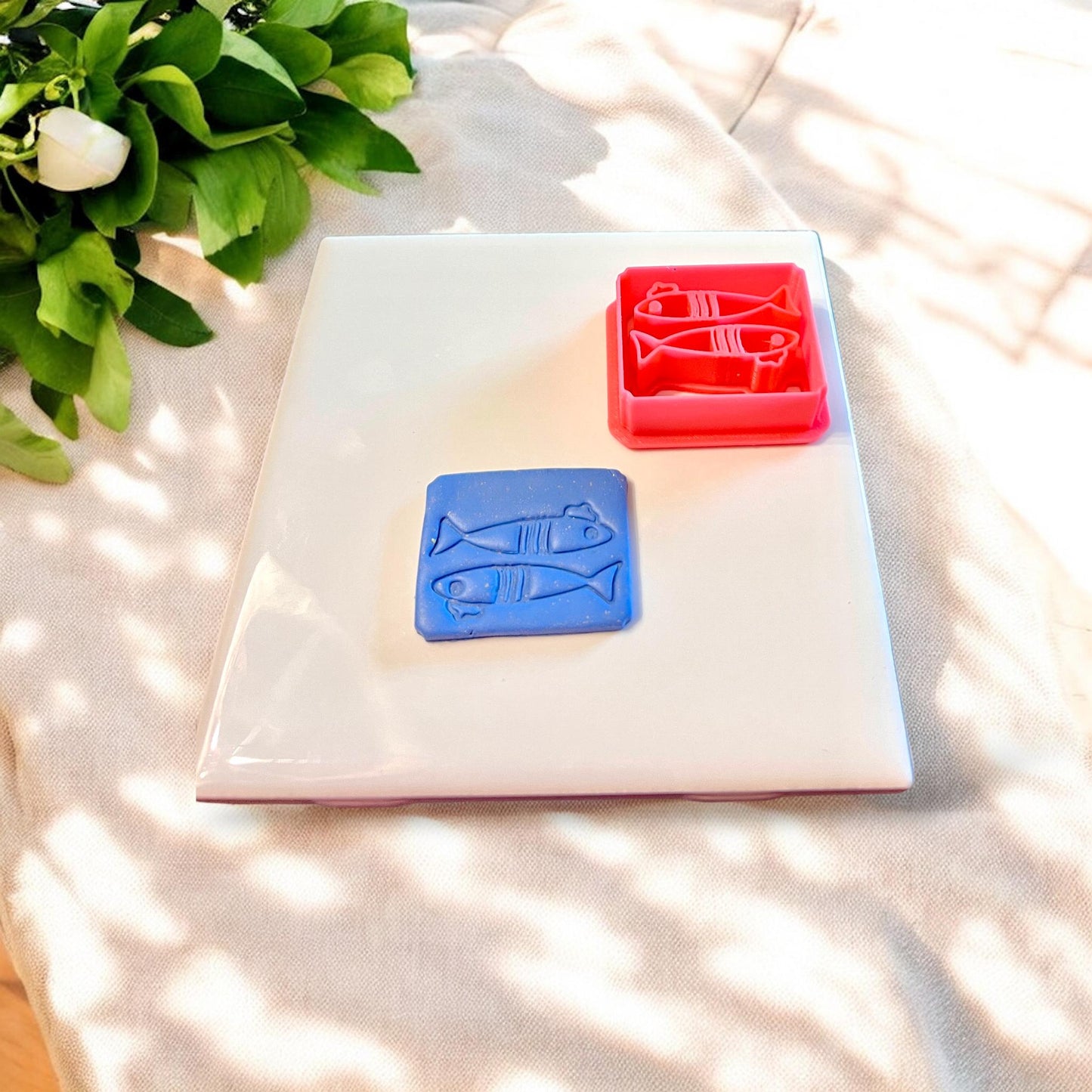 Red sardine cutter next to clay cutout, showing detailed beret hat and scale etching perfect for whimsical coastal jewelry