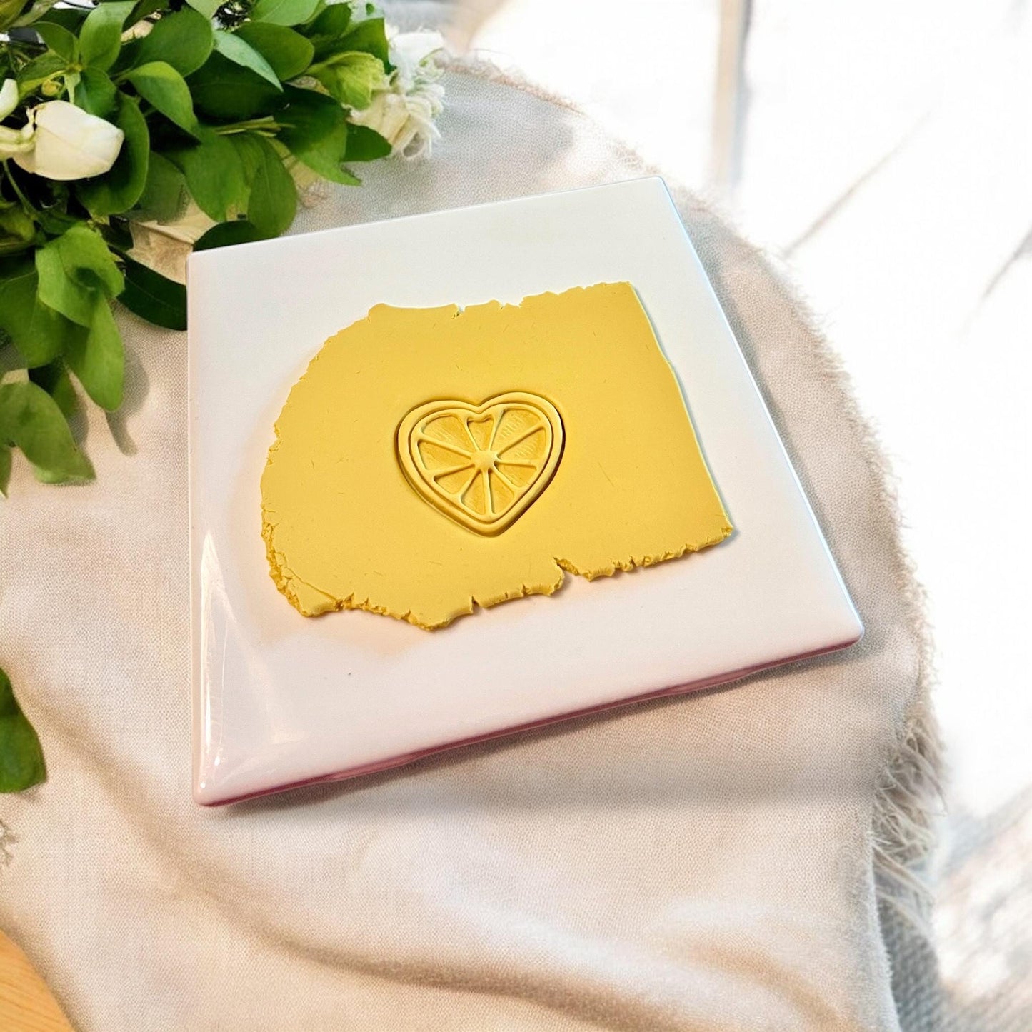 Yellow heart-shaped lime slice cutter pressed into clay with citrus embossing details