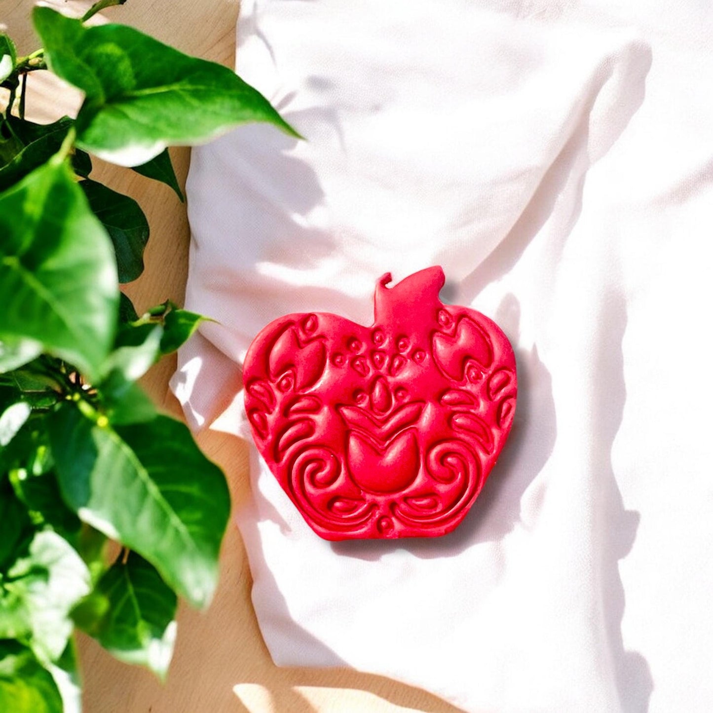 Finished folk apple clay cut lying on fabric with sunlight and greenery background