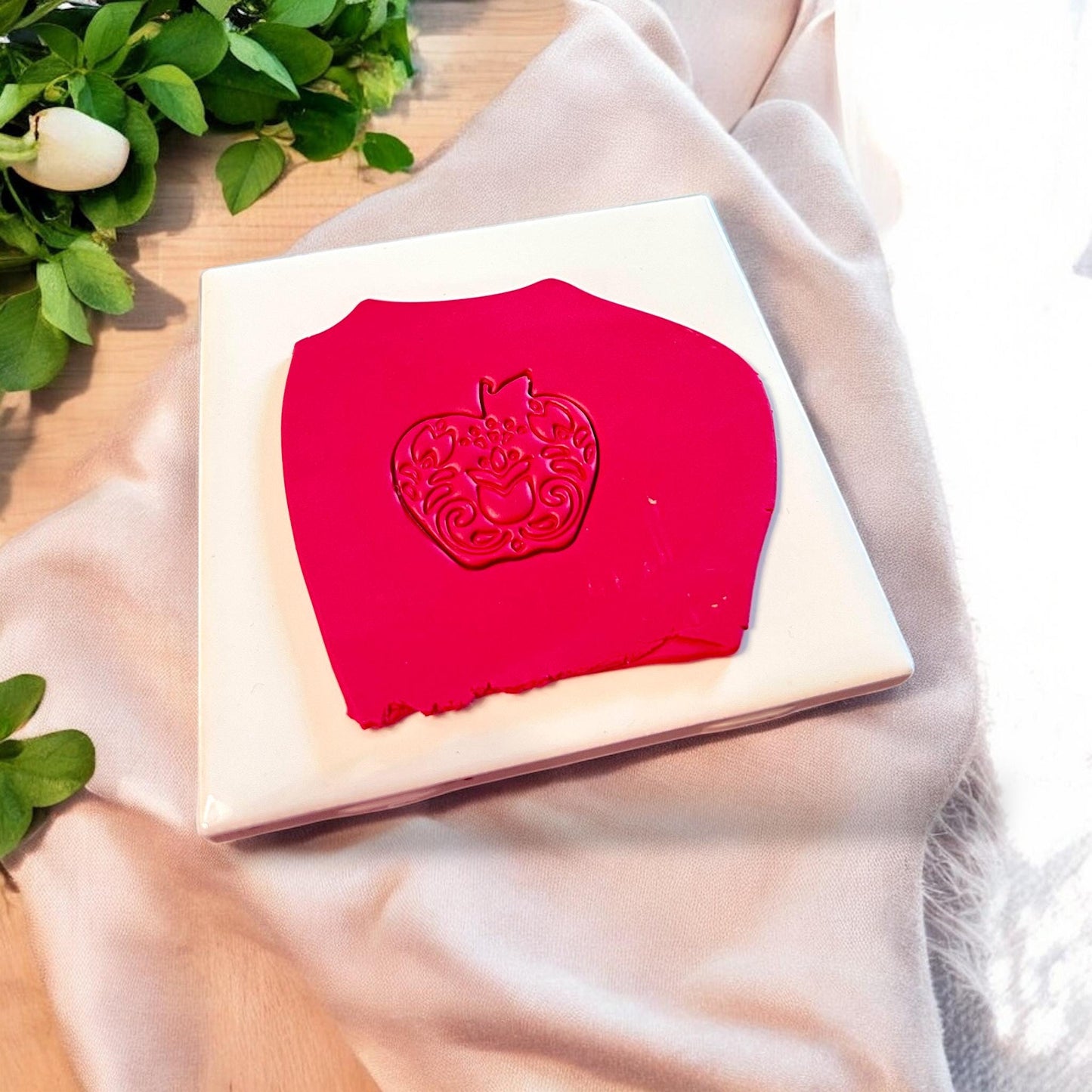 Bright red clay slab impressed with a folk art apple featuring floral and tulip detailing