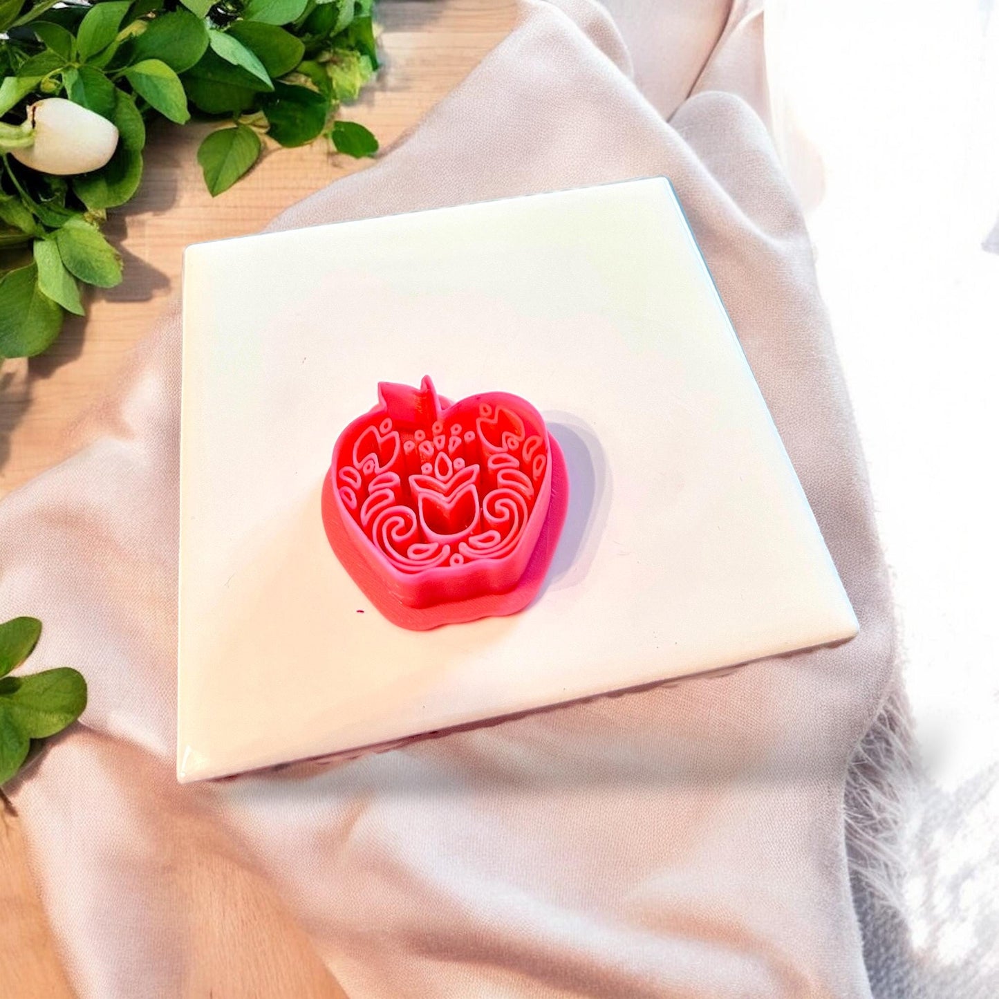 Close-up of apple-shaped cutter with floral embossing resting on white tile