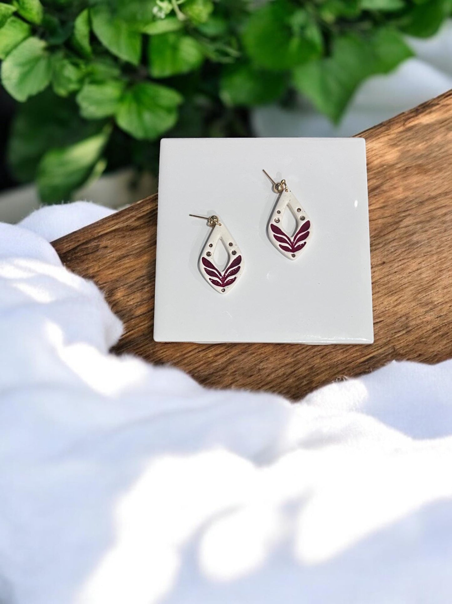 Finished pair of polymer clay earrings with embossed folk leaf design in maroon and ivory