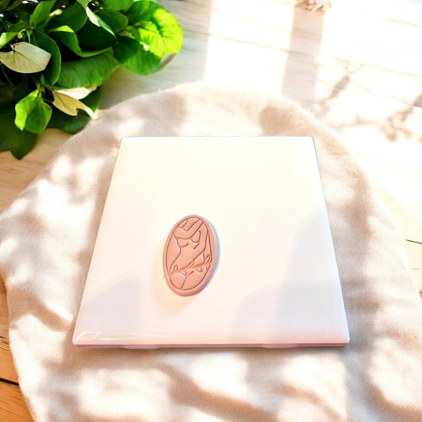Nude clay cutout of a woman’s silhouette on a smooth white tile, showcasing delicate embossed detailing.