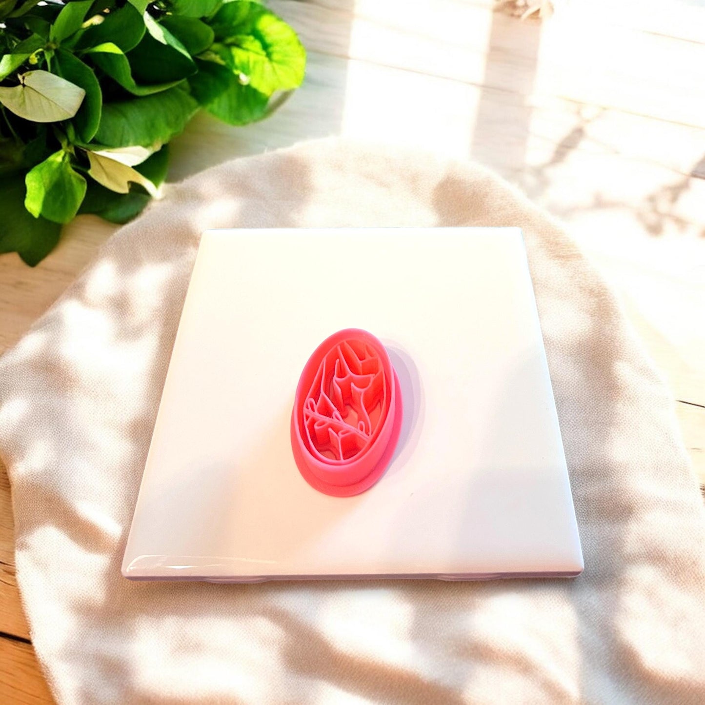 Embossed red silhouette clay cutter in oval shape sitting alone on a white ceramic slab.