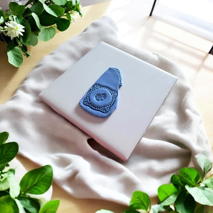 Blue clay pressed with embossed seashell earring cutter on tile with soft morning light and greenery backdrop