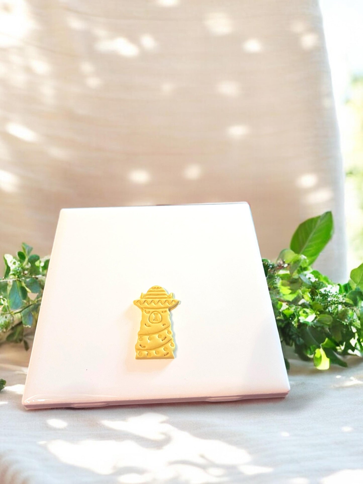 Detailed festive llama clay cutout on white tile, highlighting embossed features for dangle earrings.