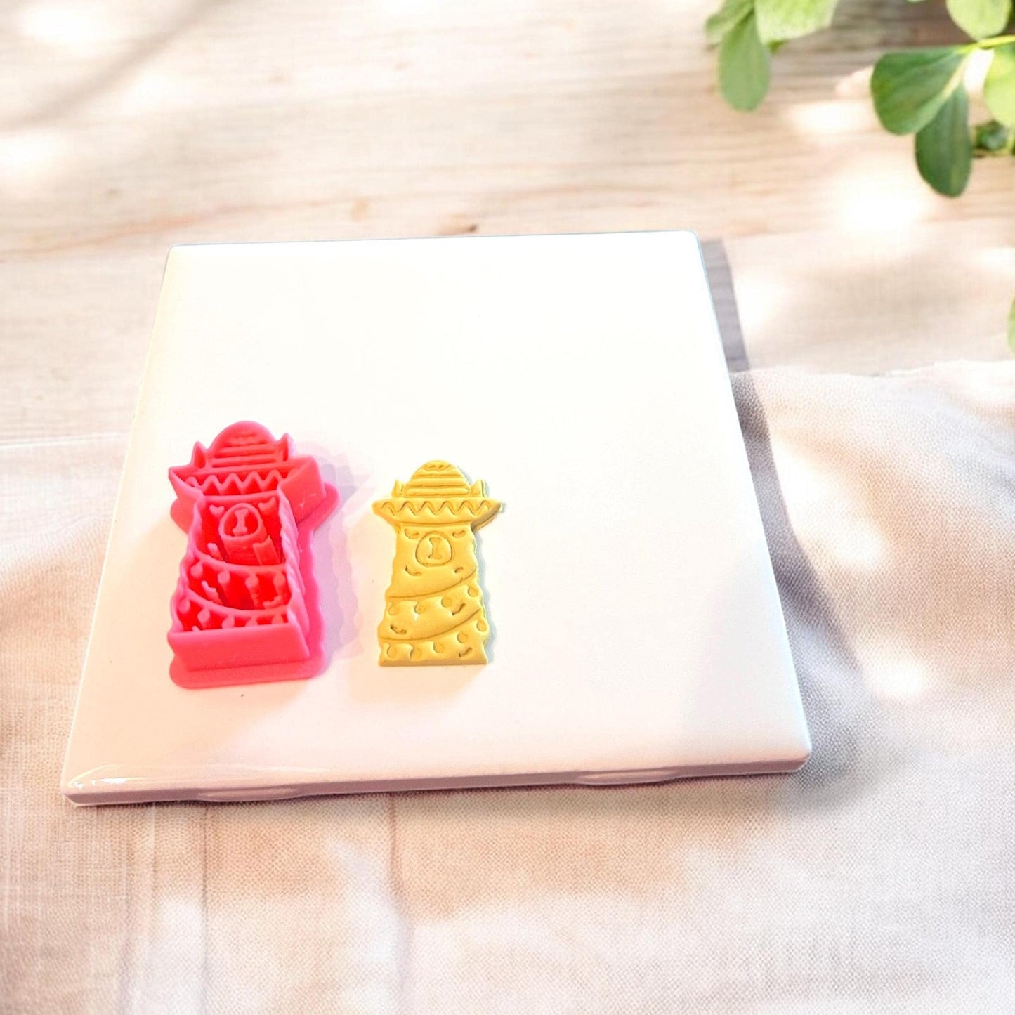 Red festive llama cutter and matching clay piece displayed together on ceramic slab with holiday props.