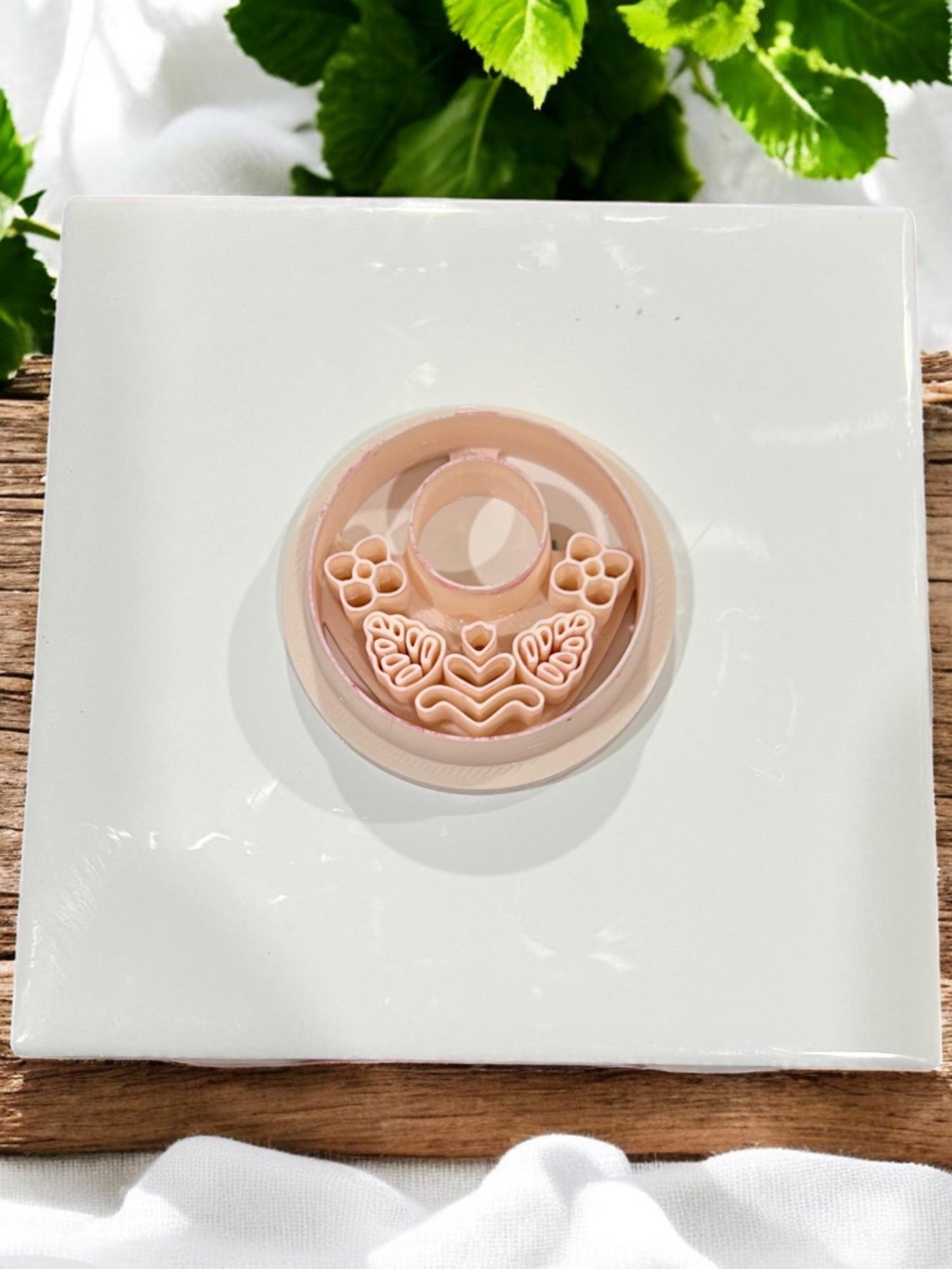 Top view of folk floral hoop polymer clay cutter in nude PLA, placed on white ceramic tile