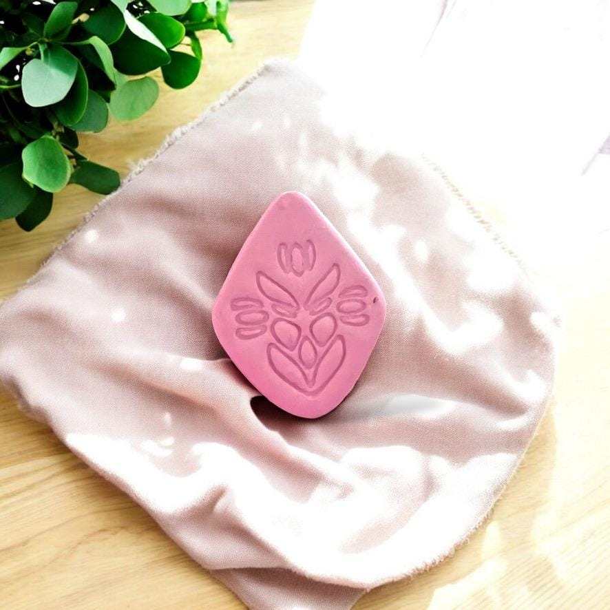 Close-up view of a folk art flower design impressed in pink clay with soft sunlight and greenery backdrop