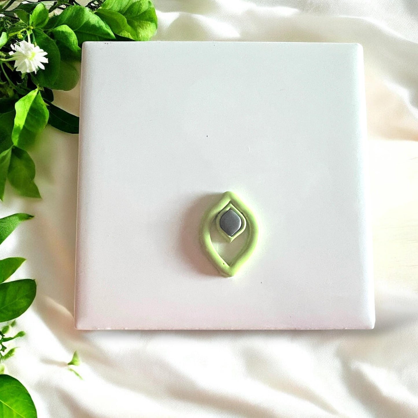 Finished green and gray jewel drop cutout pieces on a white tile surrounded by soft fabric and greenery