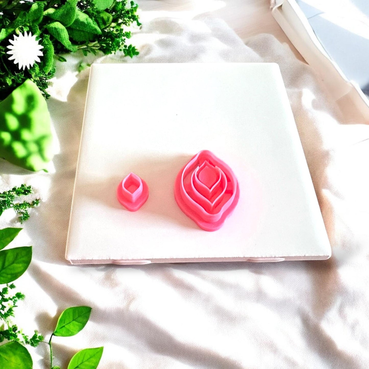 Two stacked jewel drop polymer clay cutters in bright pink color displayed on white tile with natural light and shadows