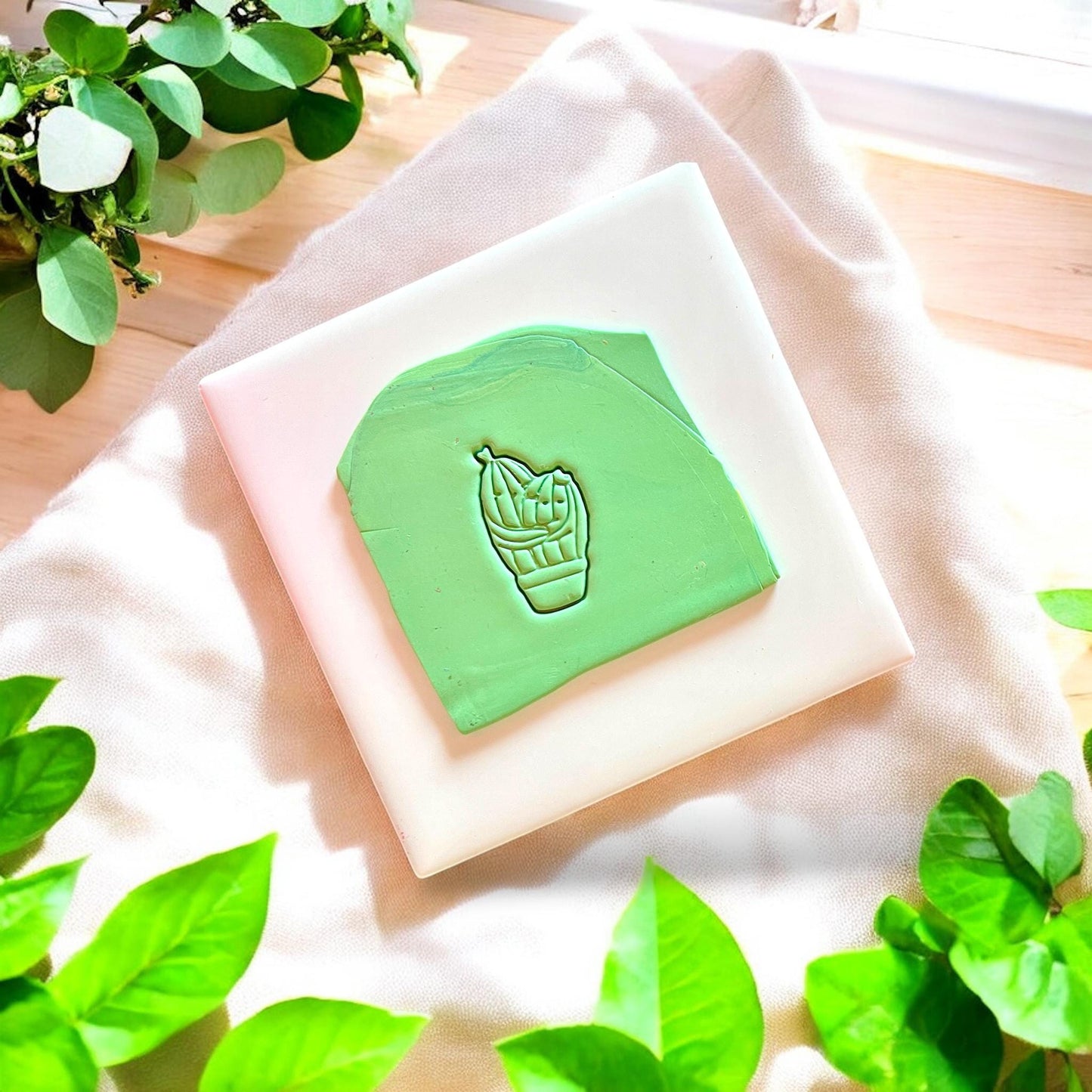 Green slab of polymer clay with a western cactus couple cutter impression on a white tile