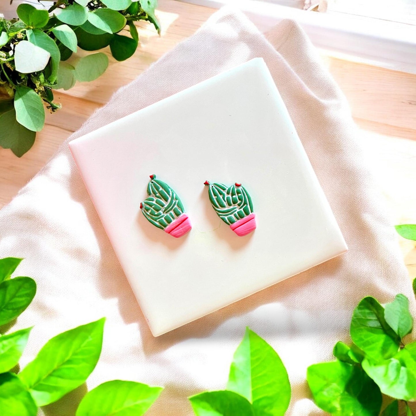 Finished polymer clay cactus couple earrings with colorful pots and red tips on white tile