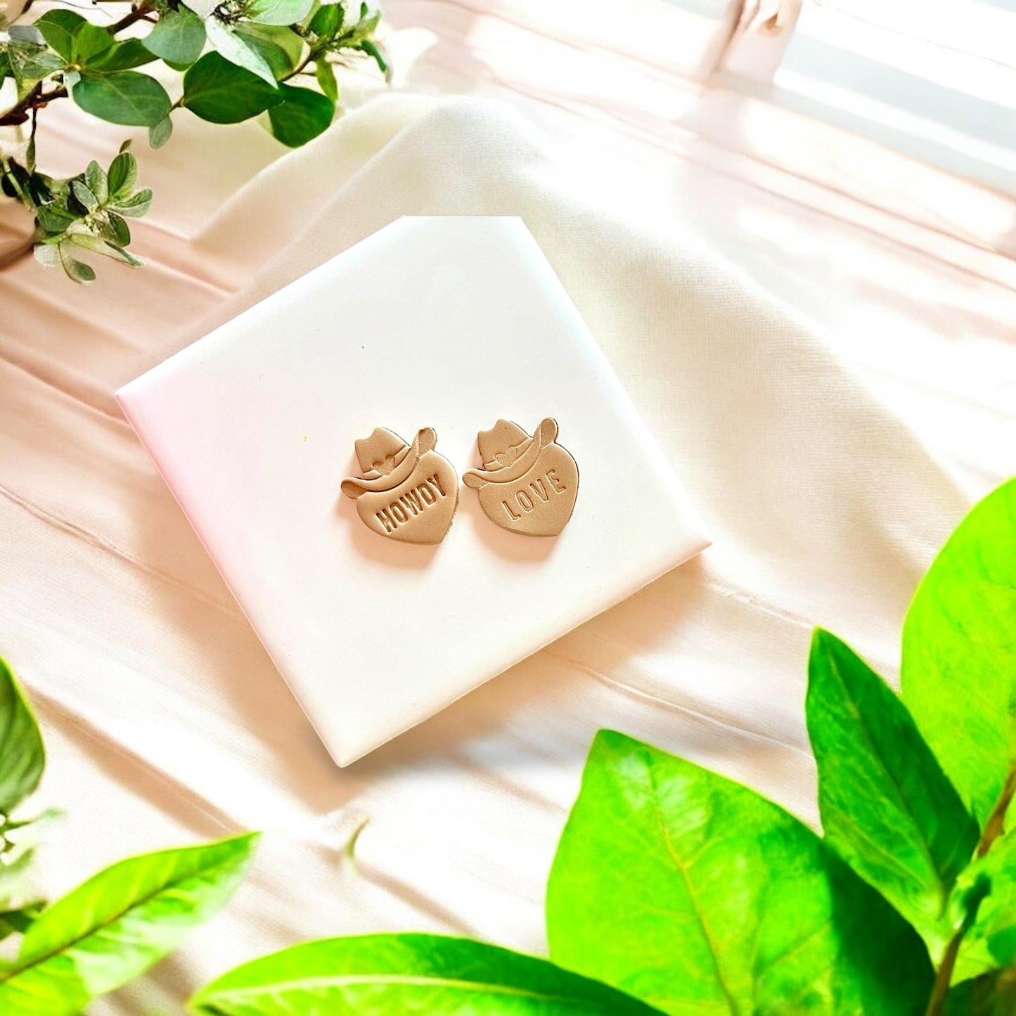 Impression of cowboy hat and heart design with "Howdy" and "Love" text on polymer clay slab, showcasing cutter detail.