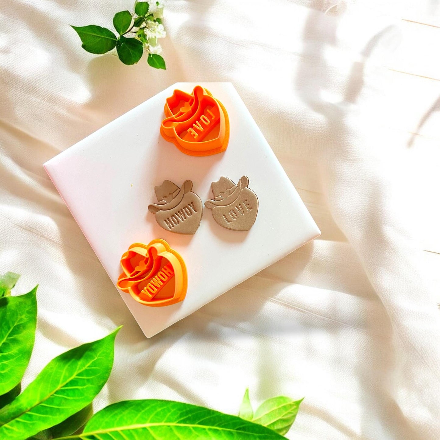 Close-up of cowboy hat and heart-shaped polymer clay cutter with "Howdy" and "Love" text, highlighting intricate design.
