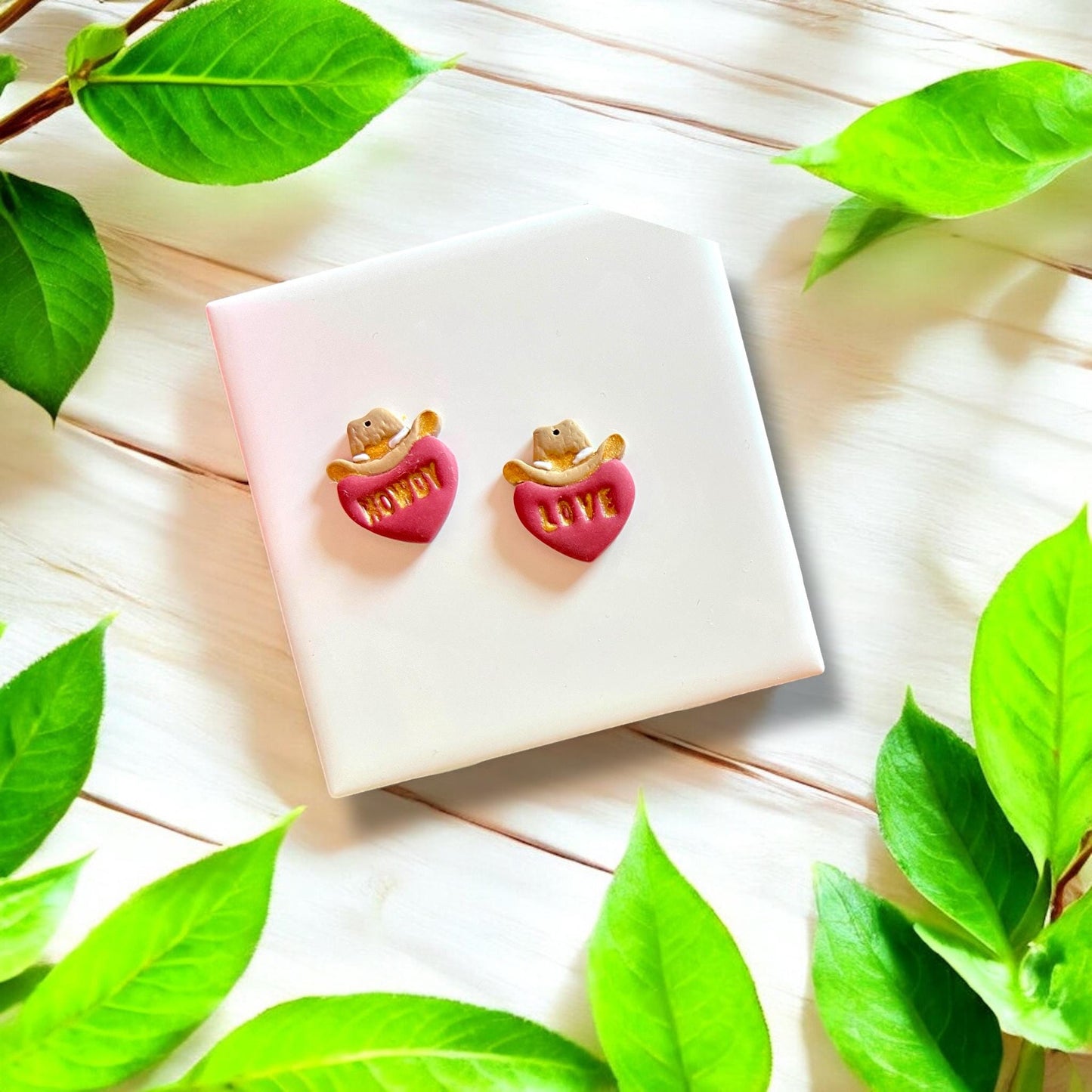 Completed polymer clay earrings in cowboy hat and heart shapes with "Howdy" and "Love" inscriptions, ideal for western-themed jewelry.