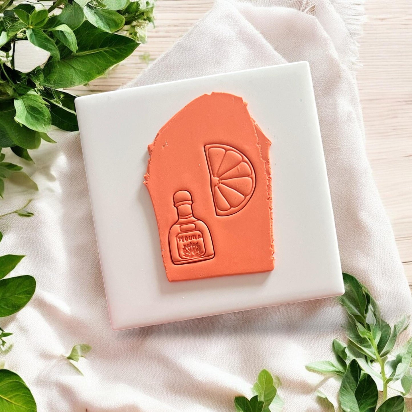 Tequila bottle and lime slice clay impressions on white slab