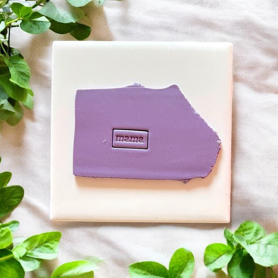 Purple clay slab with "mama" rectangle impression centered on white tile