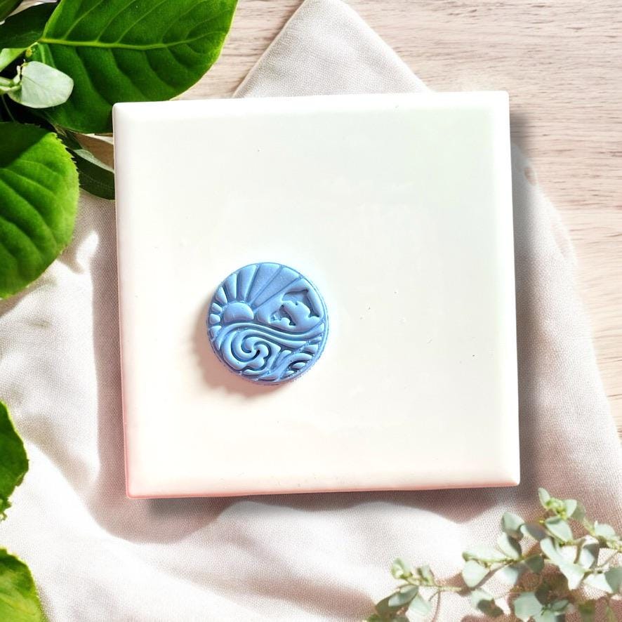 Blue clay earring with round dolphin, wave, and sun design
