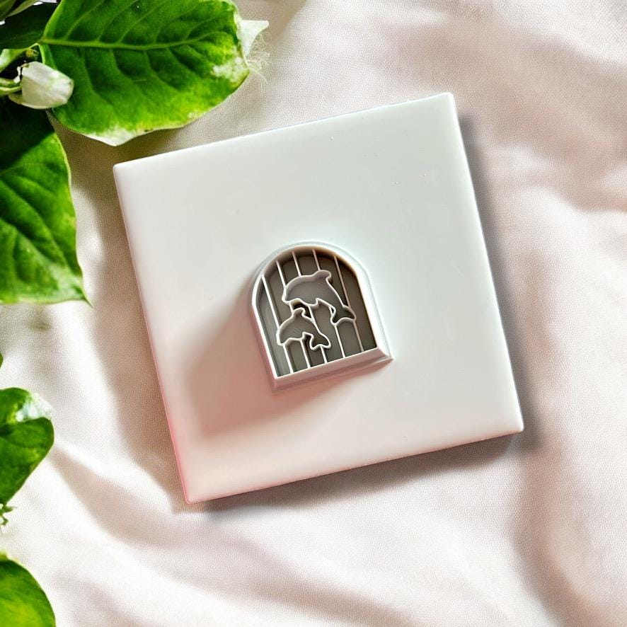 Top-down view of arch-shaped dolphin clay cutter placed on white tile