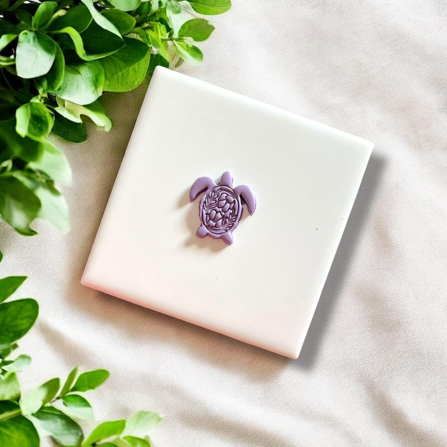 Completed purple clay turtle piece with folk art-inspired carved detailing on a white tile