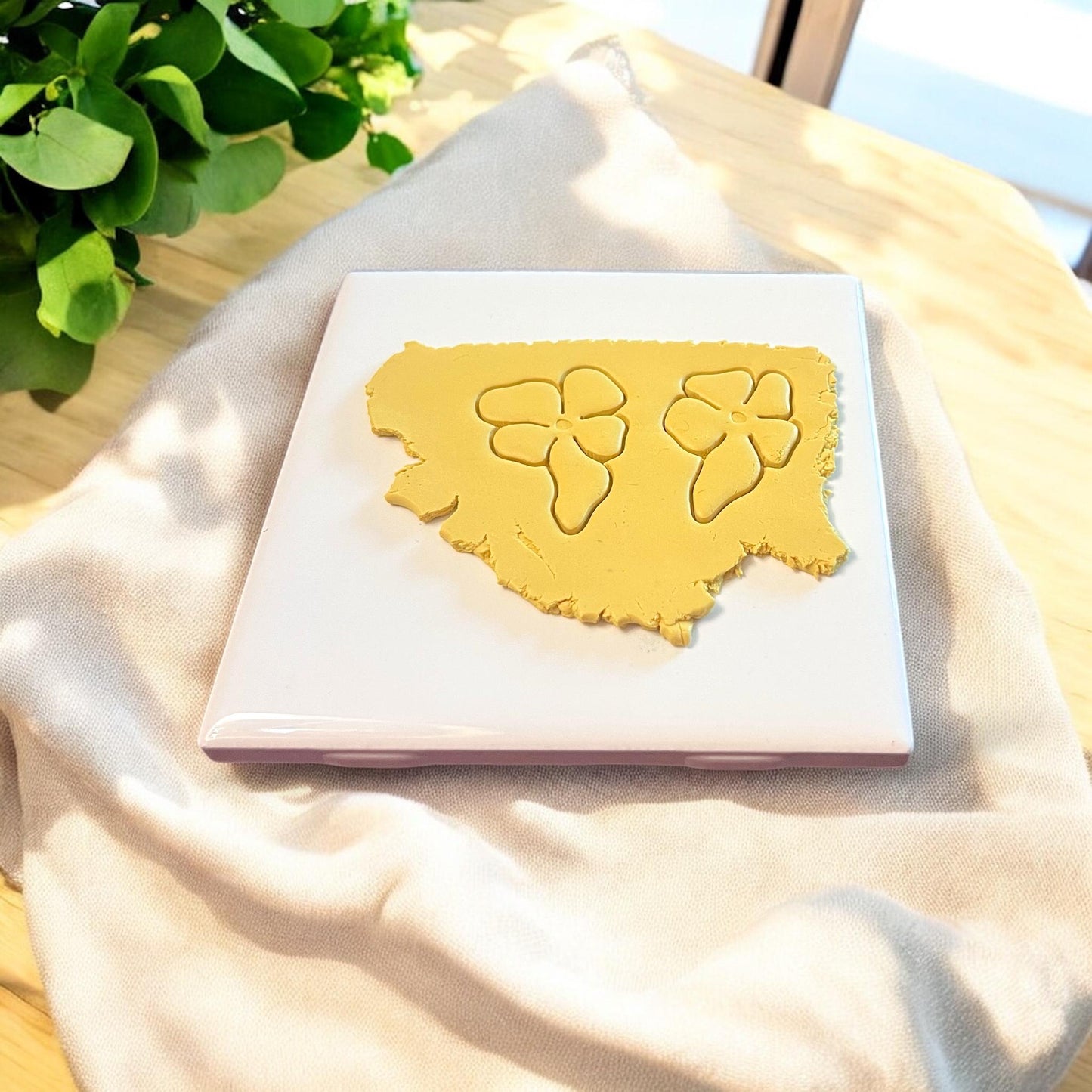 Two interlocking flower shapes cut into yellow clay using a floral polymer clay cutter, shown on a ceramic tile