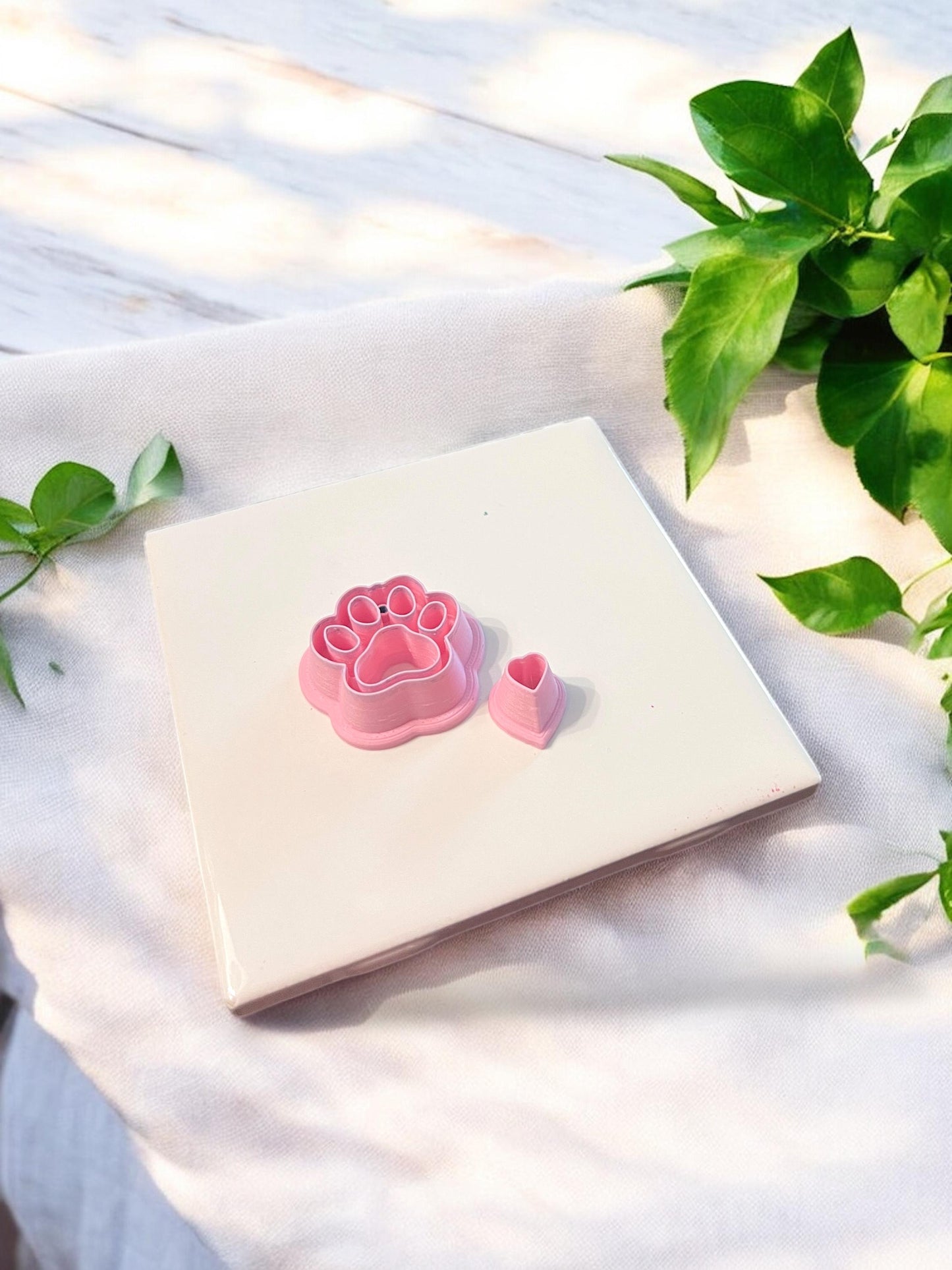 Close-up of pink polymer clay cutters: one in a paw print shape and one tiny heart cutter for clay earring creation