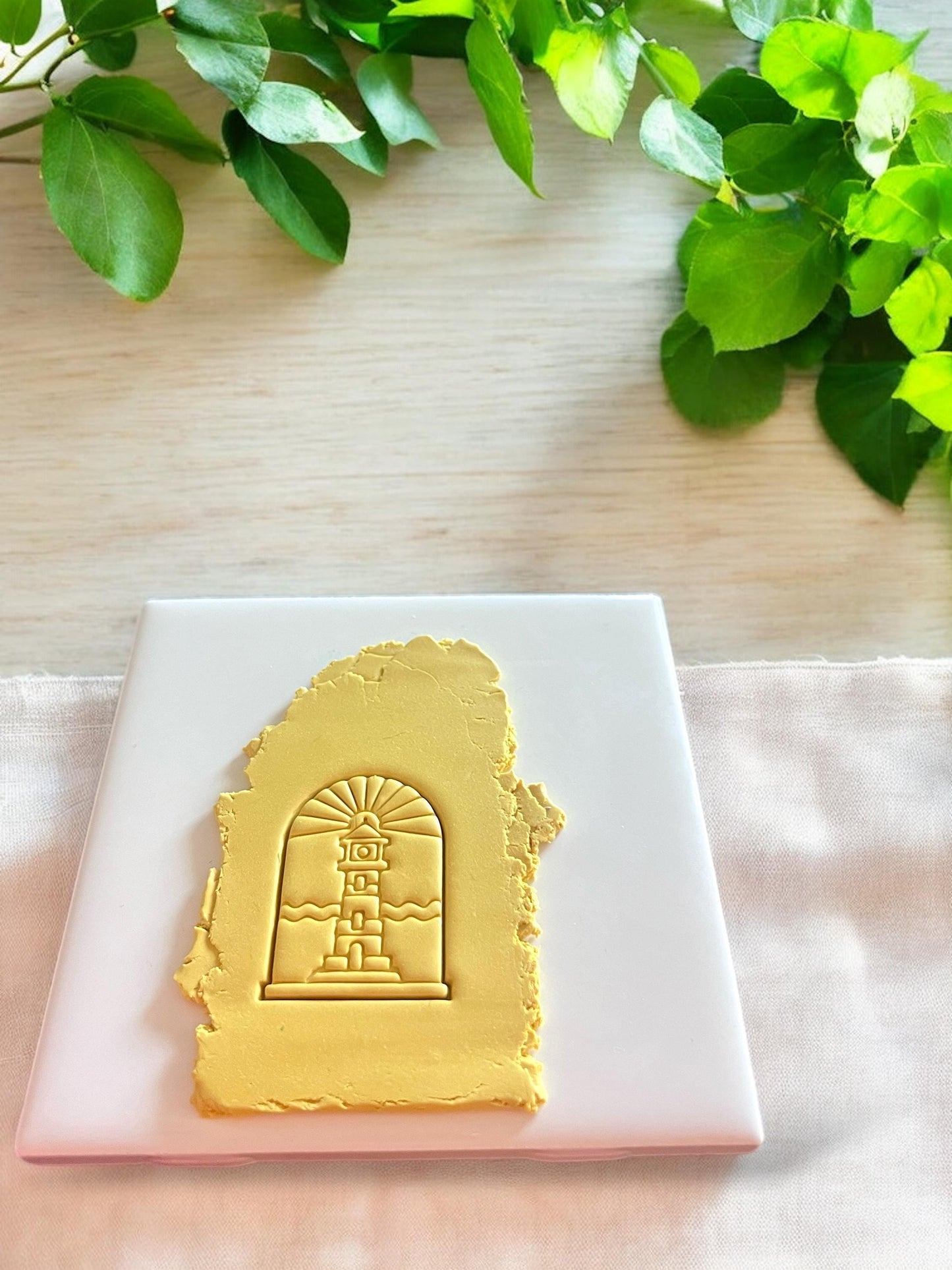 Yellow clay slab with a lighthouse scene in an arched shape pressed using a polymer clay cutter, perfect for dangles or pendants