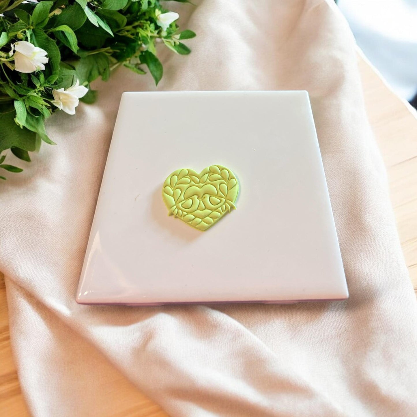 Completed clay piece in the shape of a heart with intricate love bird and floral details.