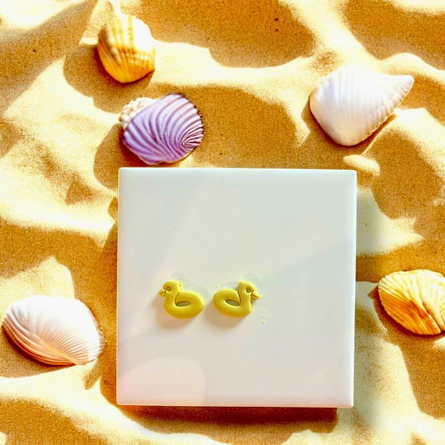 Finished clay earrings made with Duckie Pool Floatie cutter, displayed on white tile