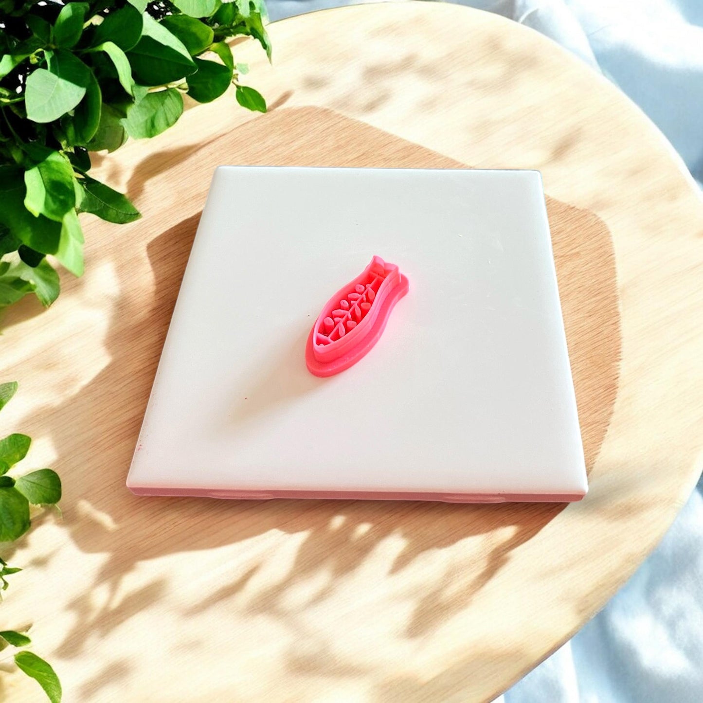 A bright red 3D printed fish-shaped cutter resting on a smooth white tile with soft lighting and shadows