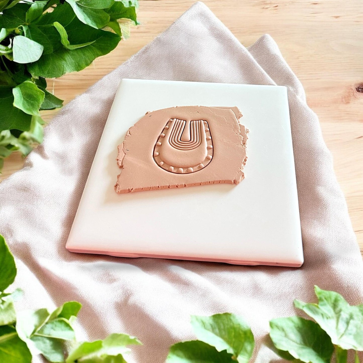 Tan polymer clay slab impressed with boho arch earring cutter showing detailed lined pattern in a soft U shape