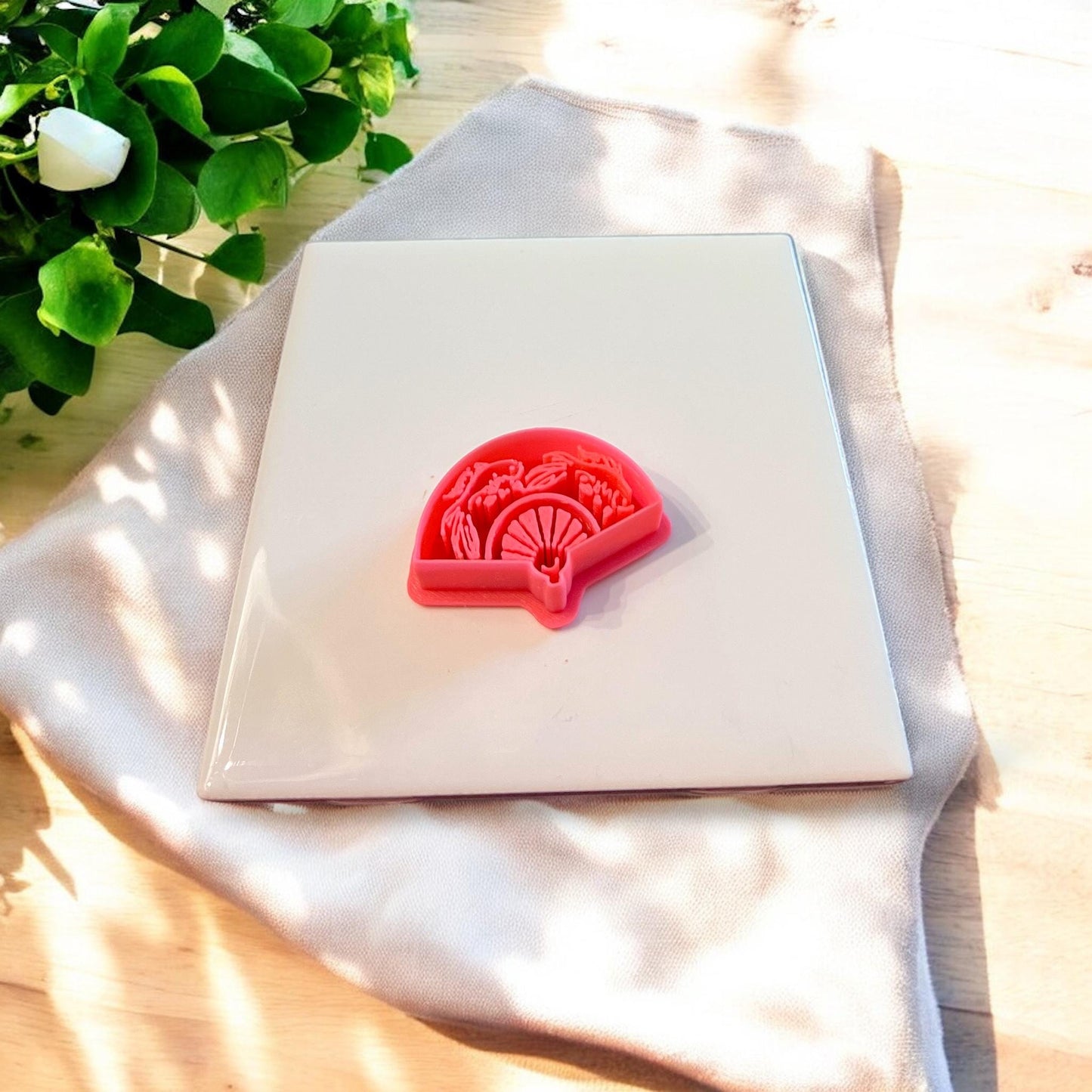 Red plastic koi fan shaped clay cutter placed on white surface with soft neutral background