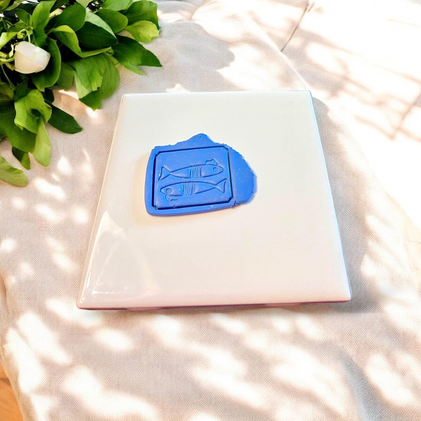 Sardine-shaped polymer clay slab with whimsical French beret detail, shown pressed into brown clay on a white tile backdrop