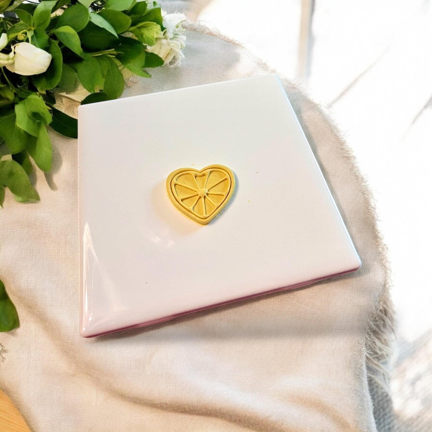 Finished yellow clay piece with heart citrus design shown on a white tile