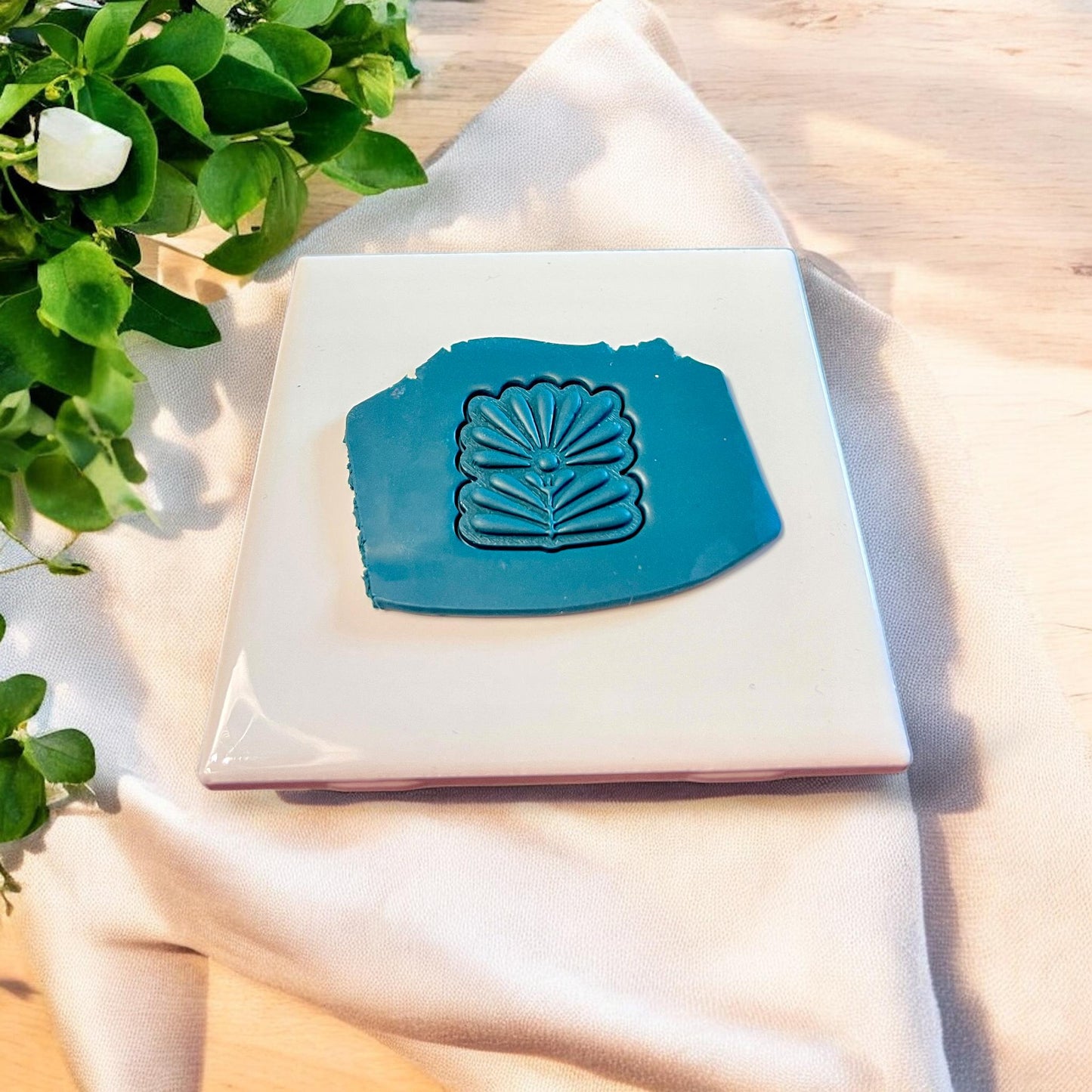 Blue slab of polymer clay featuring impression of a Scandinavian folk flower cutter with petal and line detail