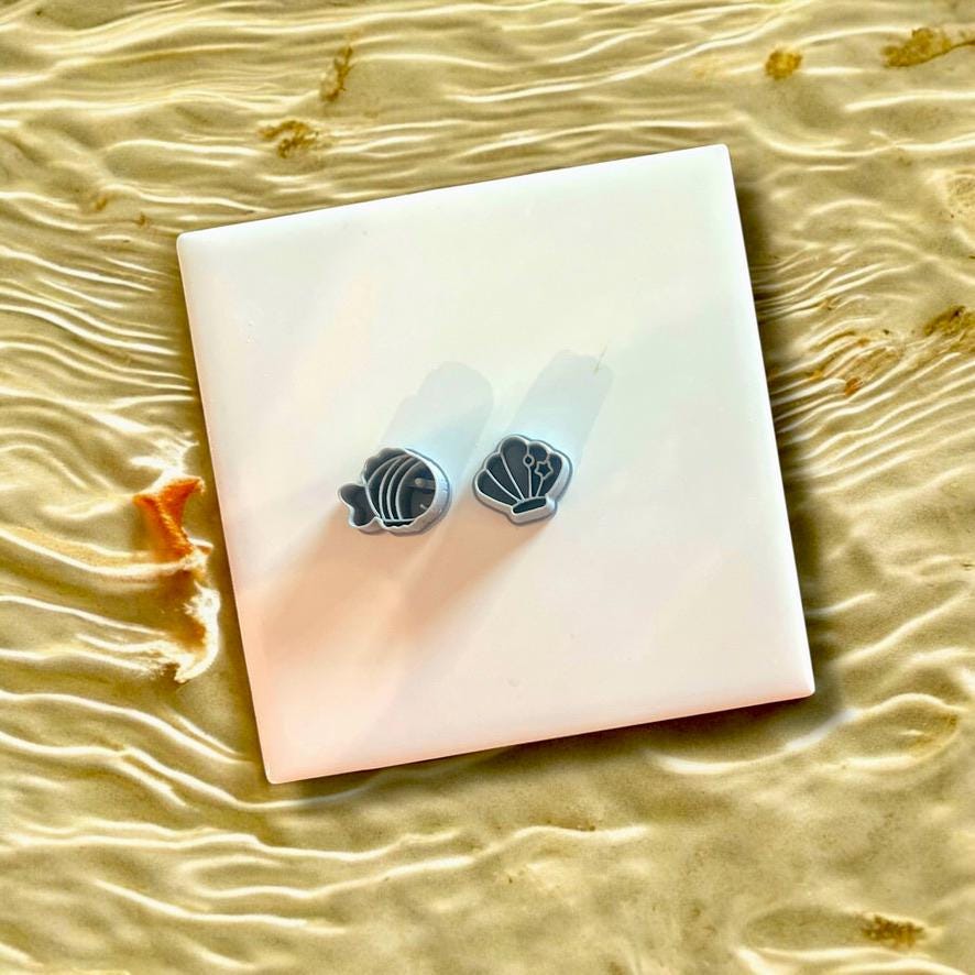 Two gray fish and shell polymer clay cutters displayed on a white tile, perfect for nautical-themed jewelry making.