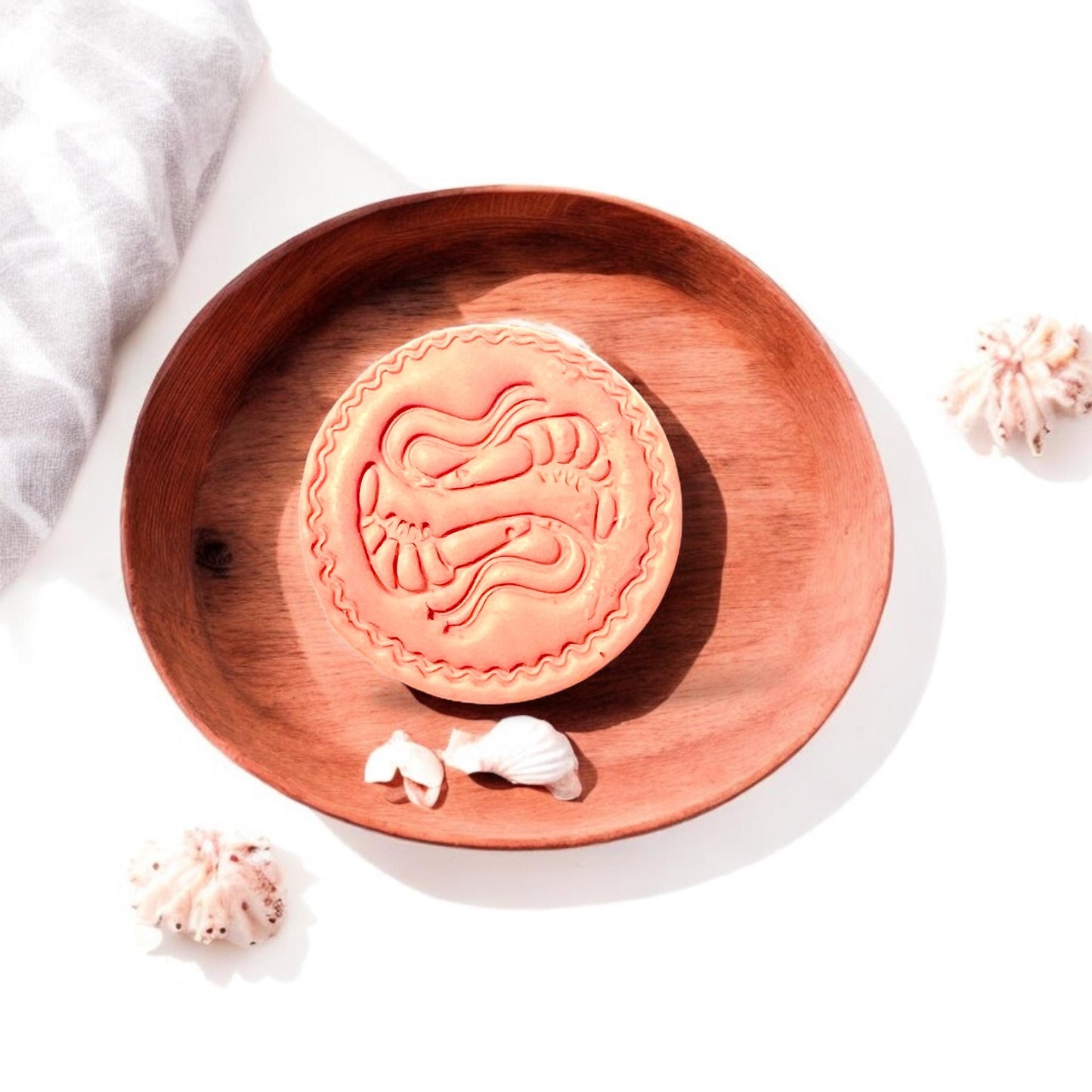 Finished shrimp clay design on wood tray surrounded by natural shells and light linen fabric.
