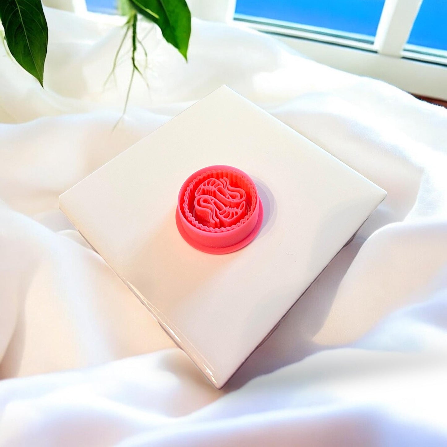 Red polymer clay cutter in shrimp shape placed on soft beige surface, emphasizing design details.