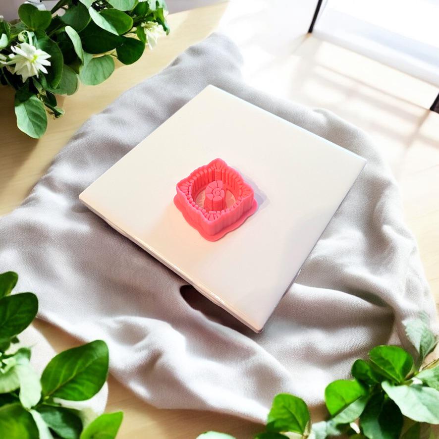 Red seashell earring cutter placed upright on a white tile, surrounded by natural morning light