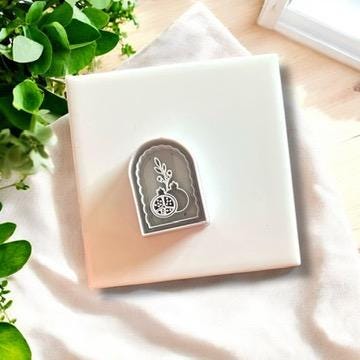 Gray pomegranate arch clay cutter displayed on a white ceramic tile, perfect for boho jewelry making.